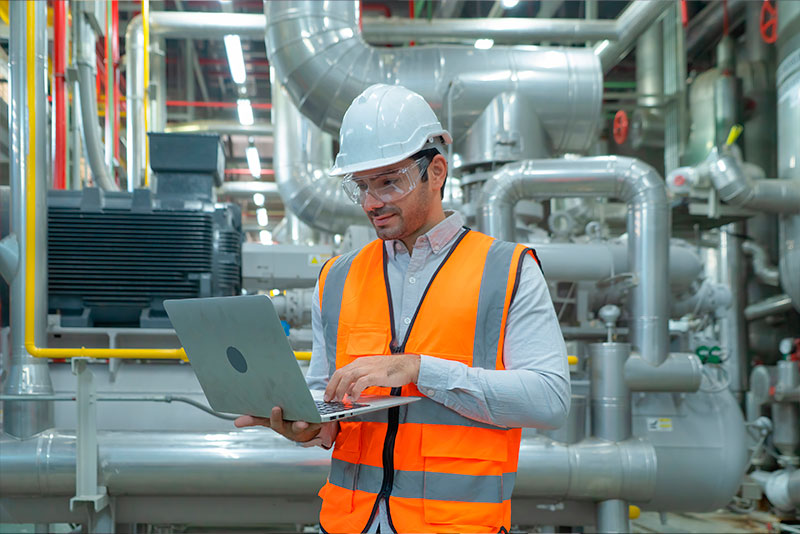 Ingeniero de Prevención de Riesgos supervisando instalaciones mirando su laptop de trabajo