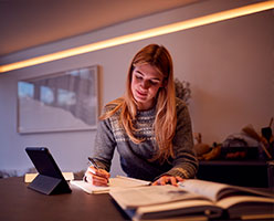 Mujer joven sentada en su escritorio escribiendo sobre un papel | Modalidad Vespertina UDLA